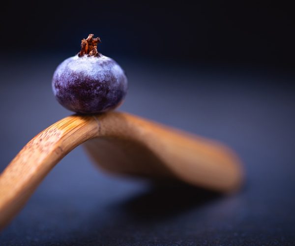 A selective focus shot of a blueberry placed on top of a wooden spoon