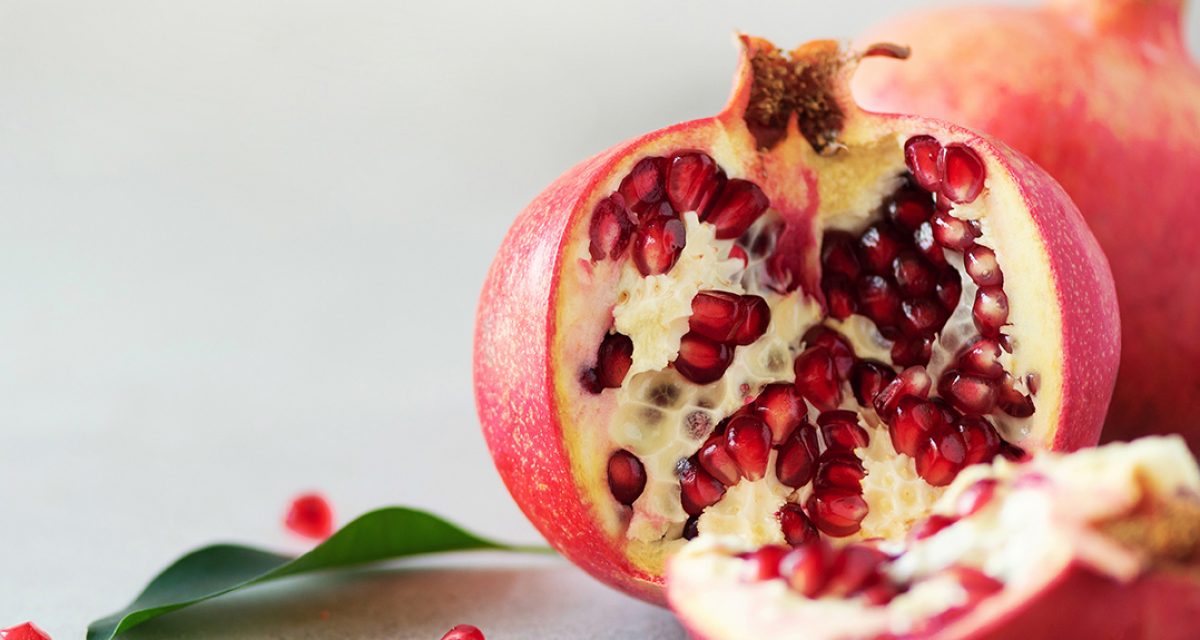 Ripe pomegranate fruit with green leaves on grey concrete background. Banner with copy space. Vegan, healthy diet concept.